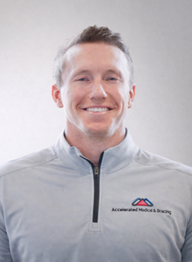 Smiling person in a light gray zip-up jacket with a logo against a plain background