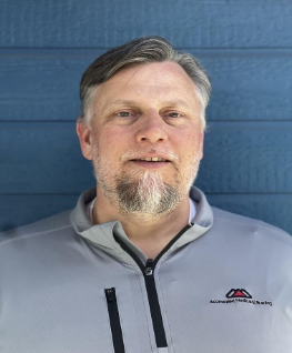 Portrait of a smiling man in a gray zip-up jacket against a blue wall