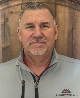 Portrait of a man in a gray zip-up jacket against a wooden background