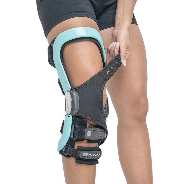Person wearing a turquoise and black knee brace on a bent leg.