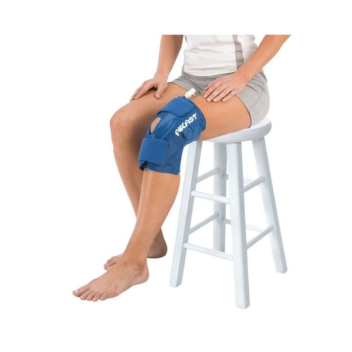 Person seated on stool wearing blue knee brace on left leg