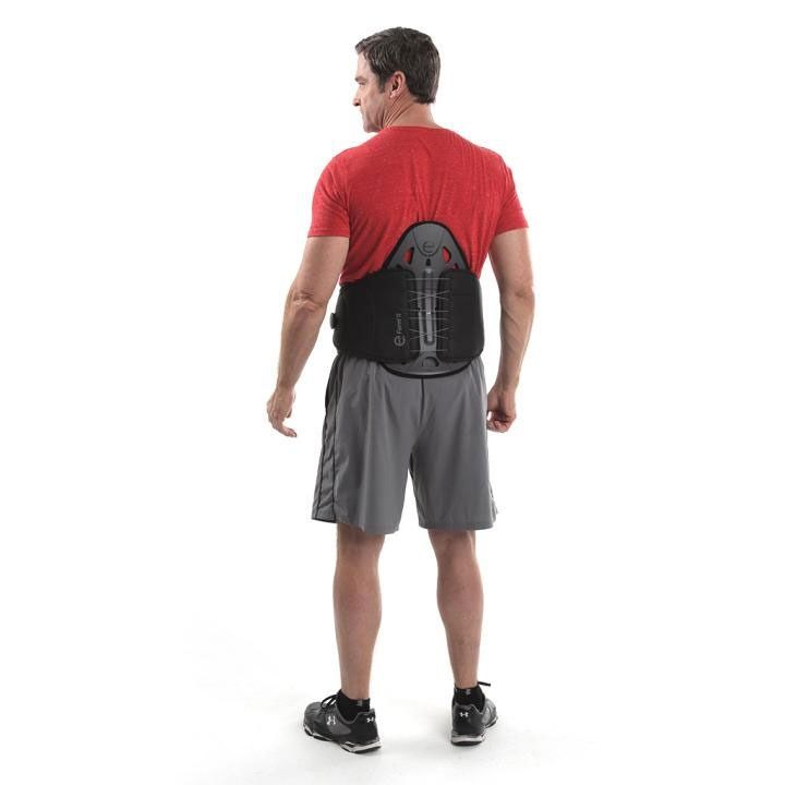 Man wearing a red shirt and gray shorts with a black back brace, standing against a white background