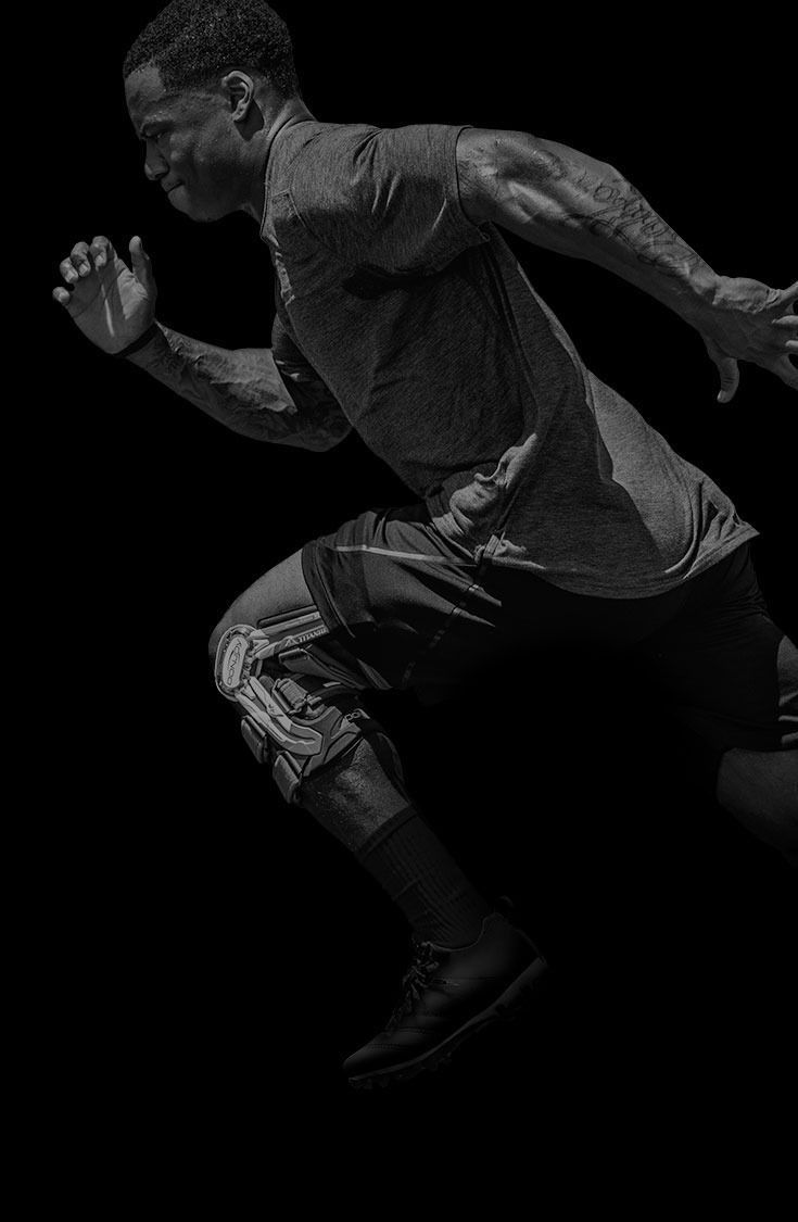 Athlete sprinting in profile against a black background, wearing dark training gear.