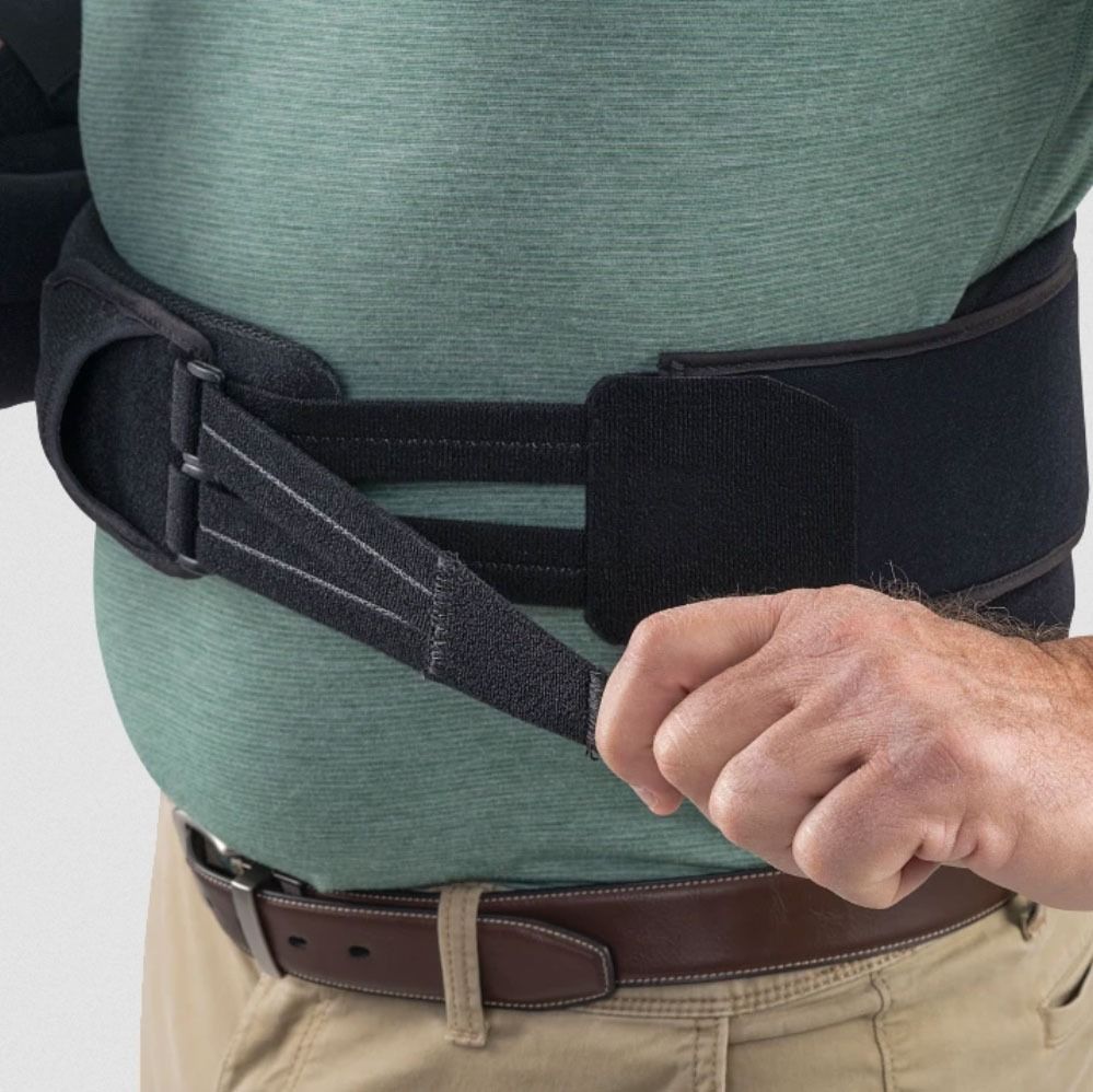 Person tightening a black back brace around a green shirt and beige pants