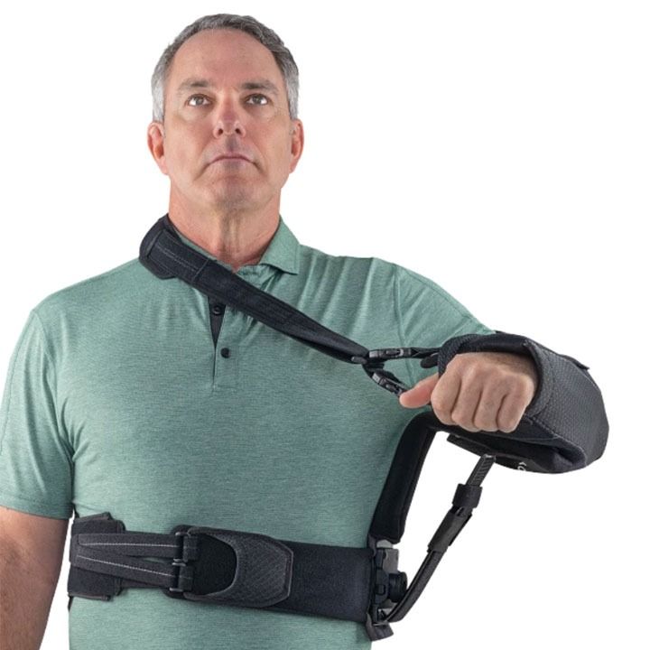 Man in green polo wearing an arm sling and waist support brace against a white background
