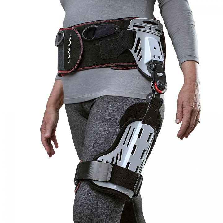 Person wearing a black and silver orthopedic leg brace and waist support belt