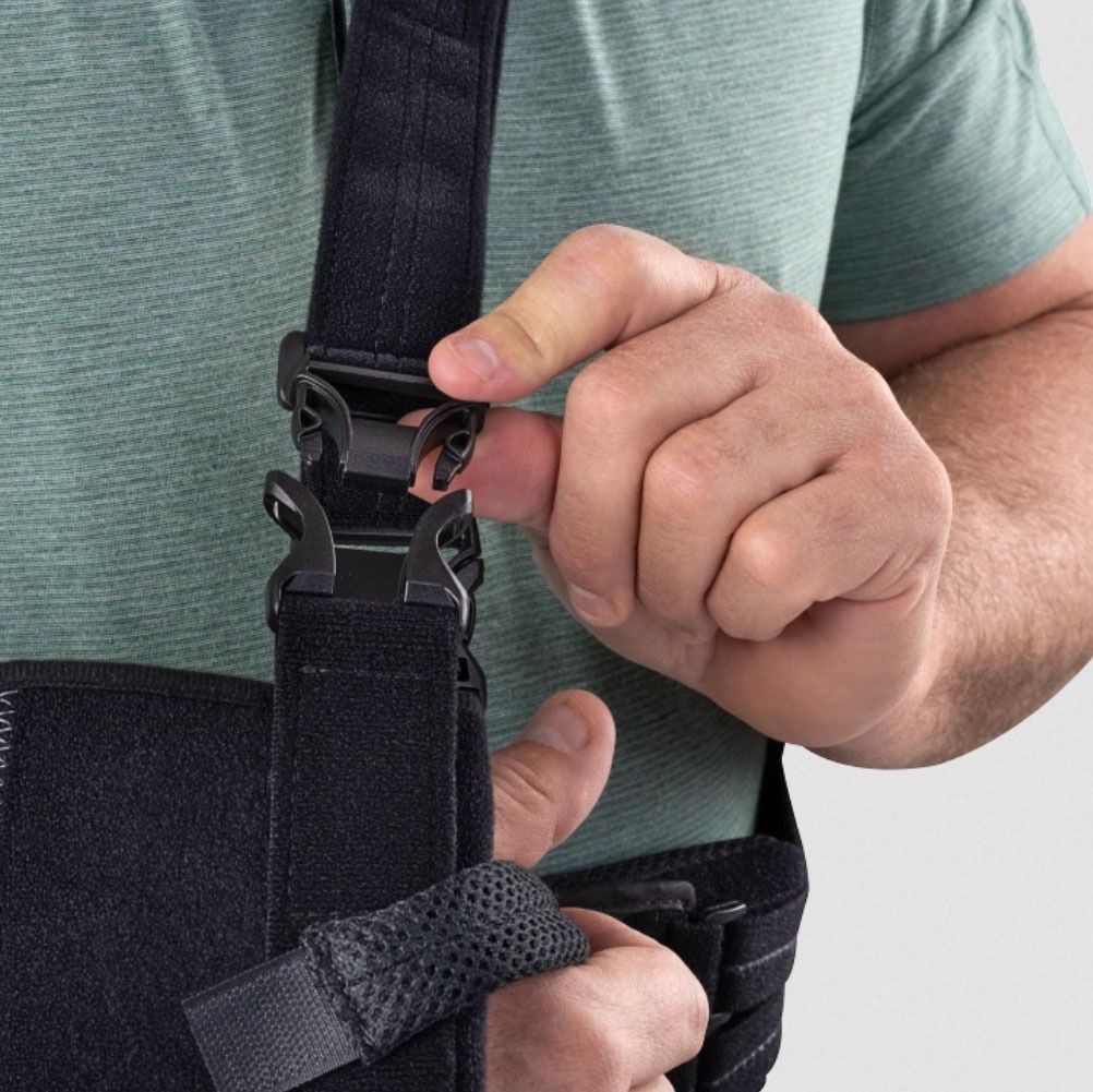 Close-up of hands clipping a black shoulder strap on a support brace