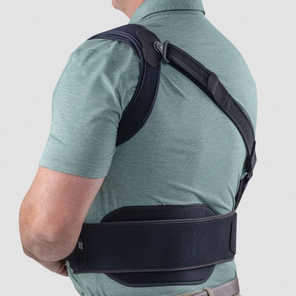 Person wearing a black shoulder and back brace over a green shirt, viewed from the side.