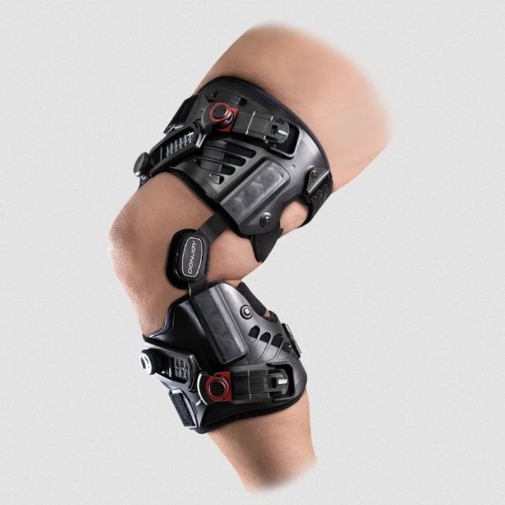 Black orthopedic knee brace with adjustable straps on a bent knee, shown on a white background