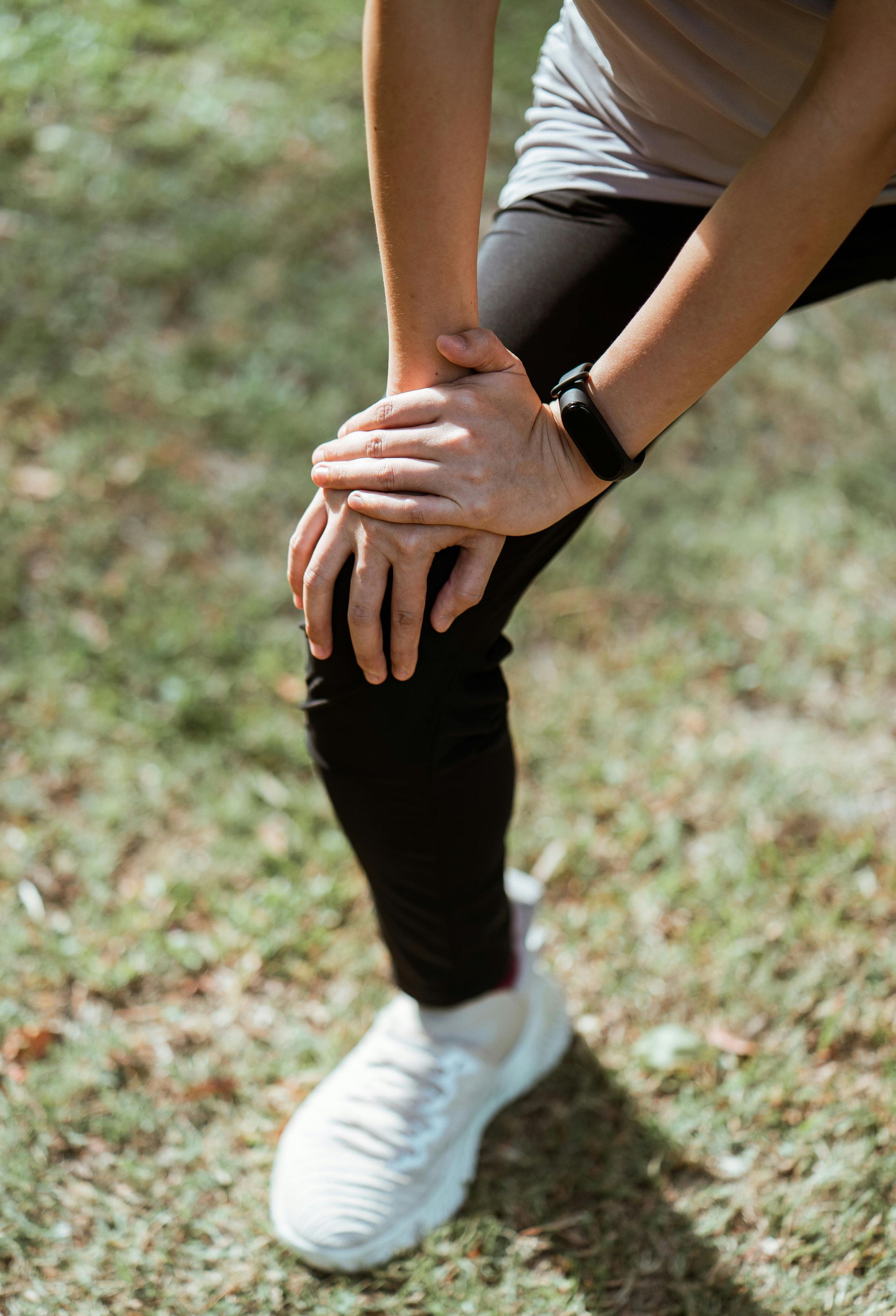 Person crouching outdoors, clutching one knee with a smartwatch on the wrist.
