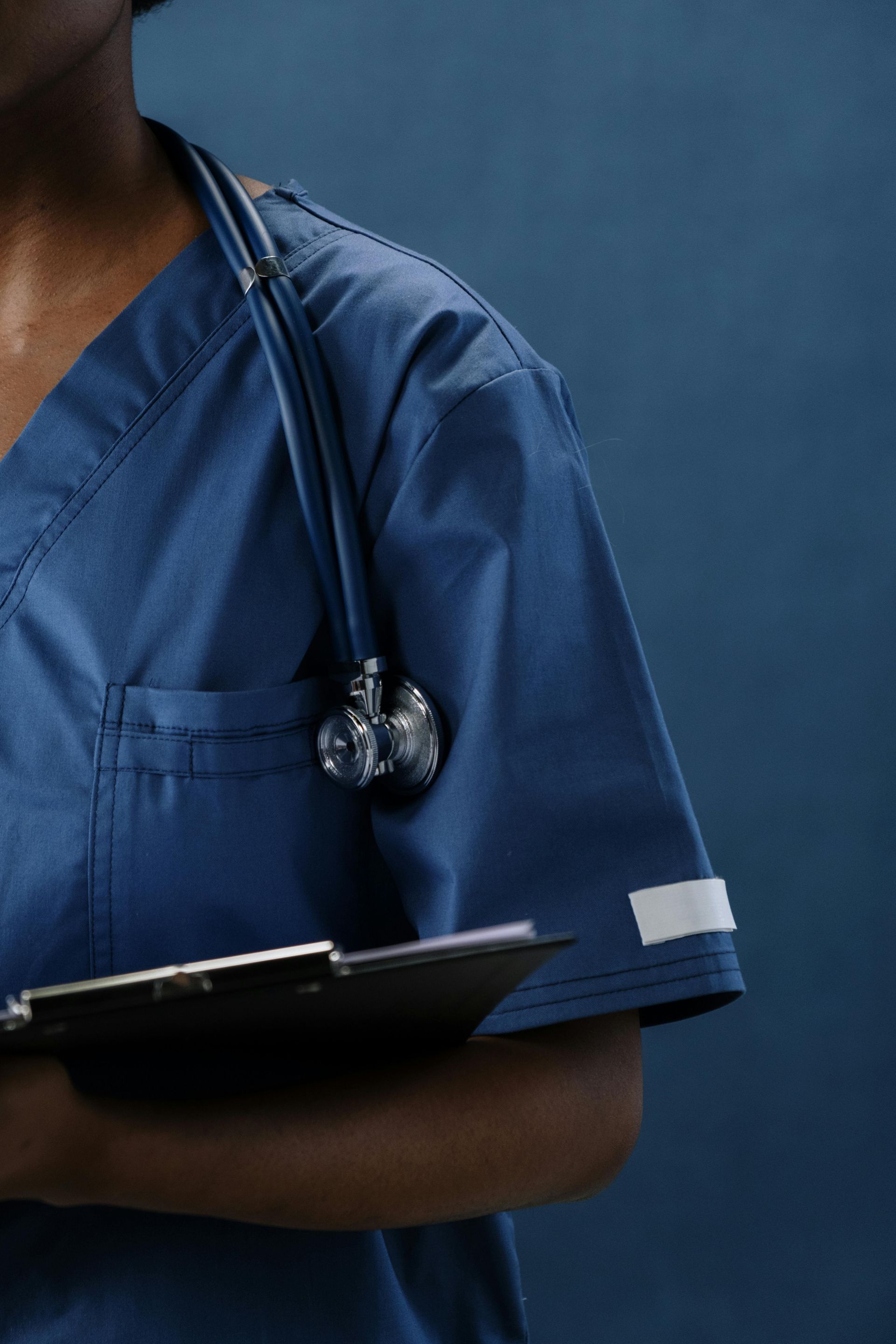 Blue-scrub nurse holding a clipboard with a stethoscope around the neck