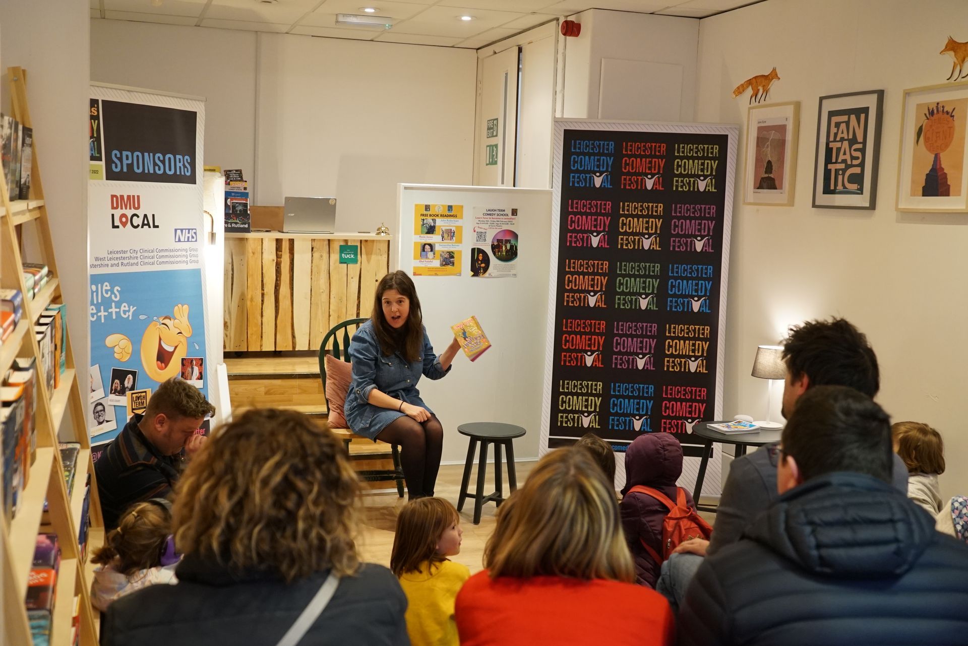 Woman reading a book to a group in a brightly lit bookstore setting.