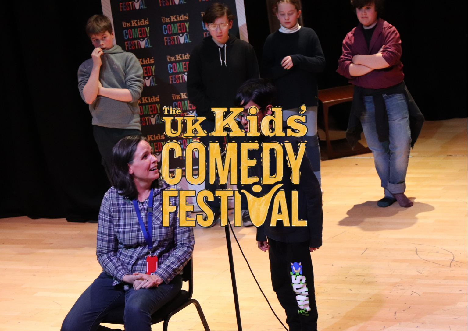 Woman seated, talking to boy with microphone on stage; other people in background.