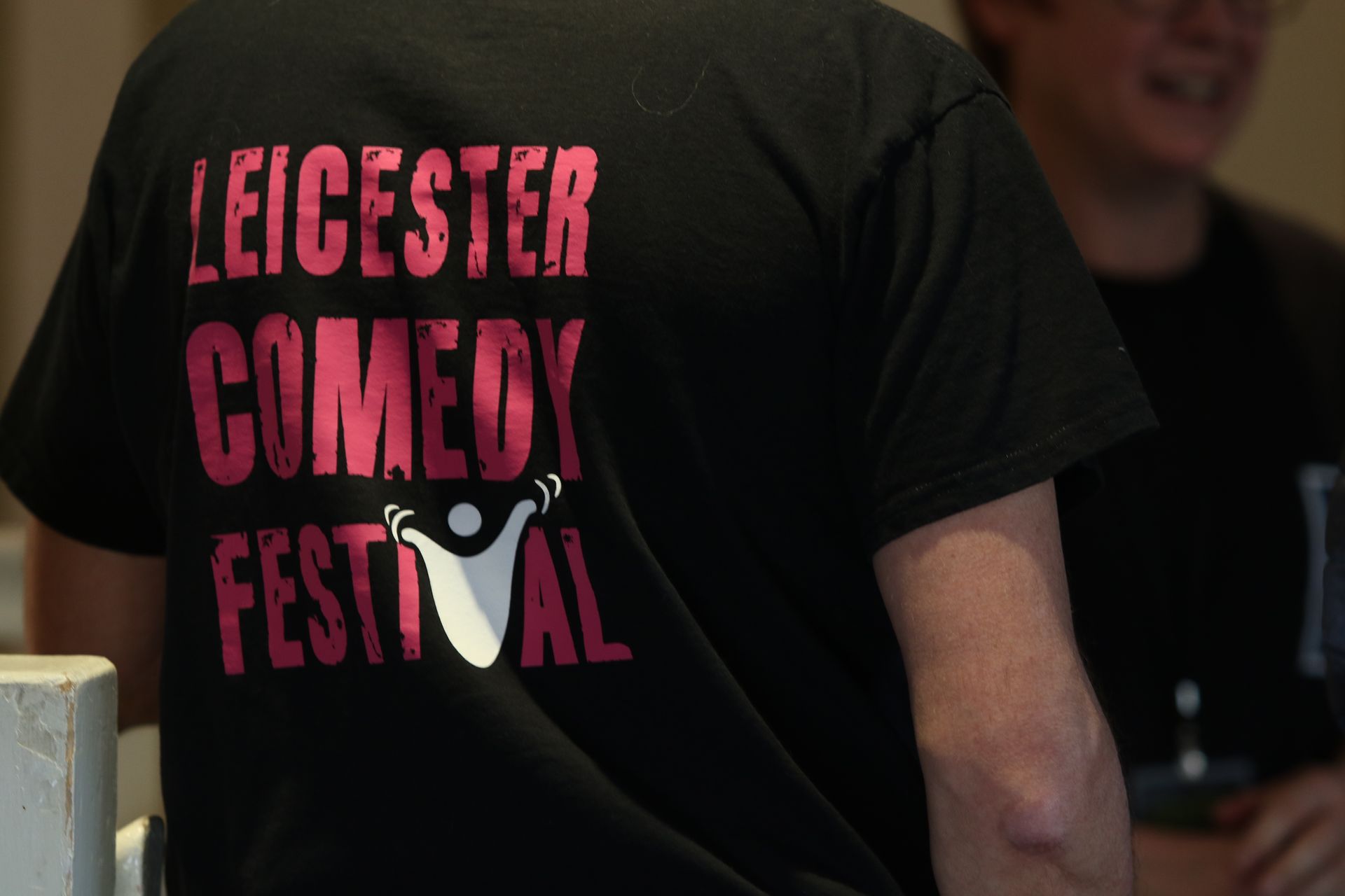 Man wearing a black Leicester Comedy Festival t-shirt, with pink text and logo on the back.