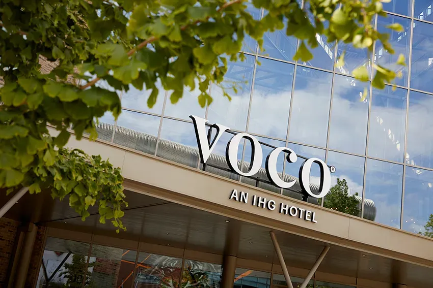 VOCO hotel sign, with blue sky and tree branches in the background.