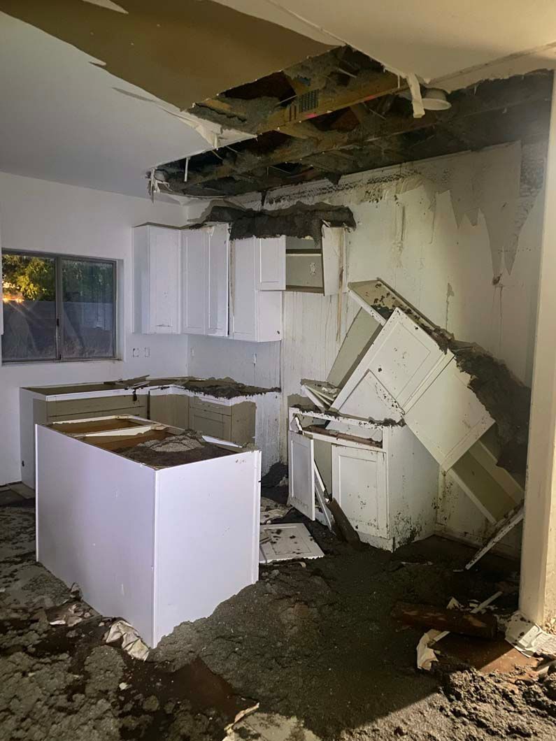 A kitchen with a broken ceiling and a broken refrigerator.