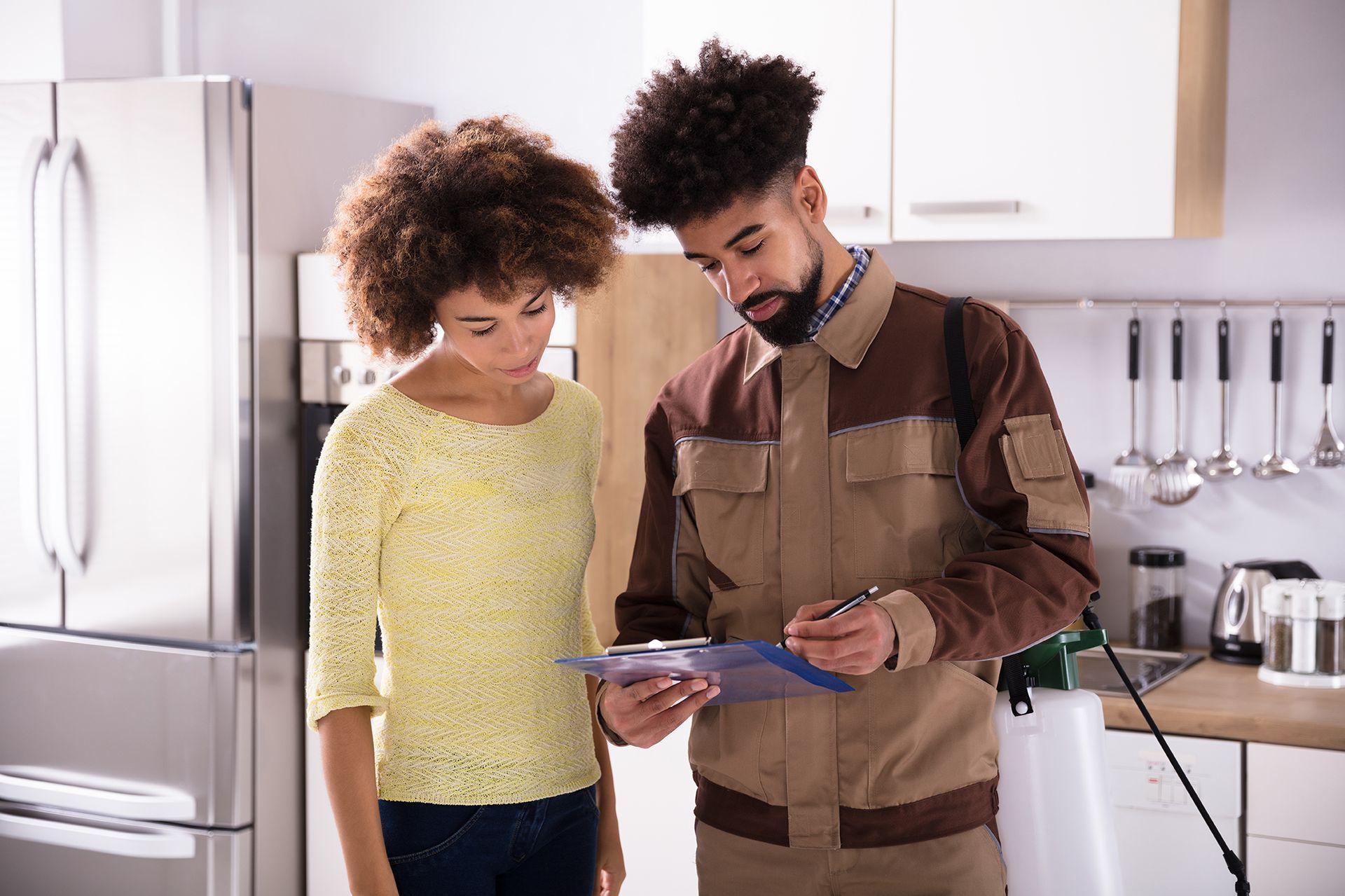 Man in uniform and woman looking at clipboard in a kitchen.