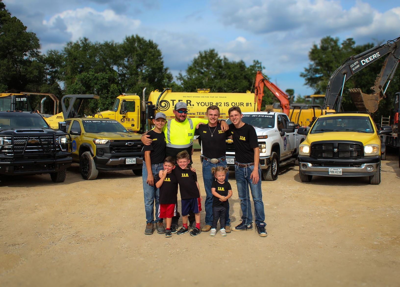 A group of people are posing for a picture in front of yellow trucks.