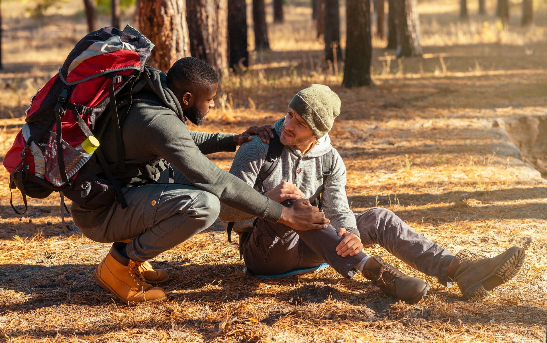 A man is helping another man who is laying on the ground in the woods.
