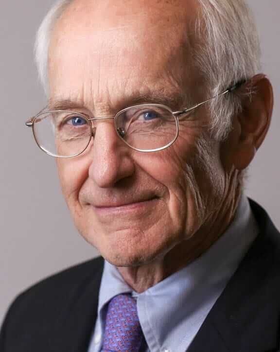 A man wearing glasses and a suit and tie is smiling for the camera.