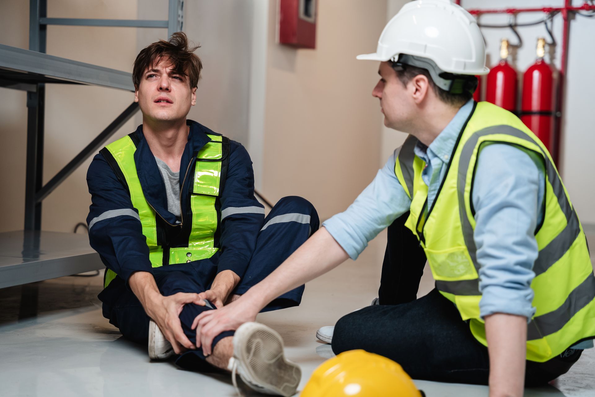 Two construction workers are sitting on the floor talking to each other.
