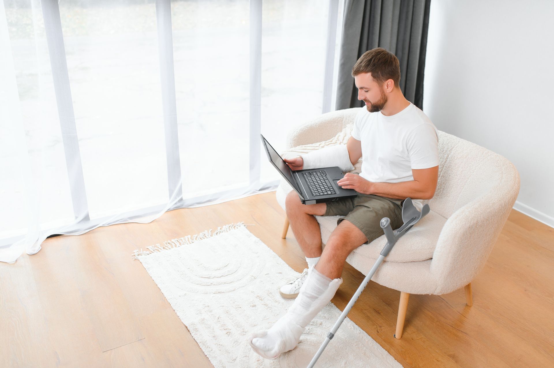 A man with a broken leg is sitting in a chair using a laptop computer.