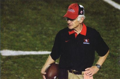 A man wearing a red hat and a black shirt holds a football