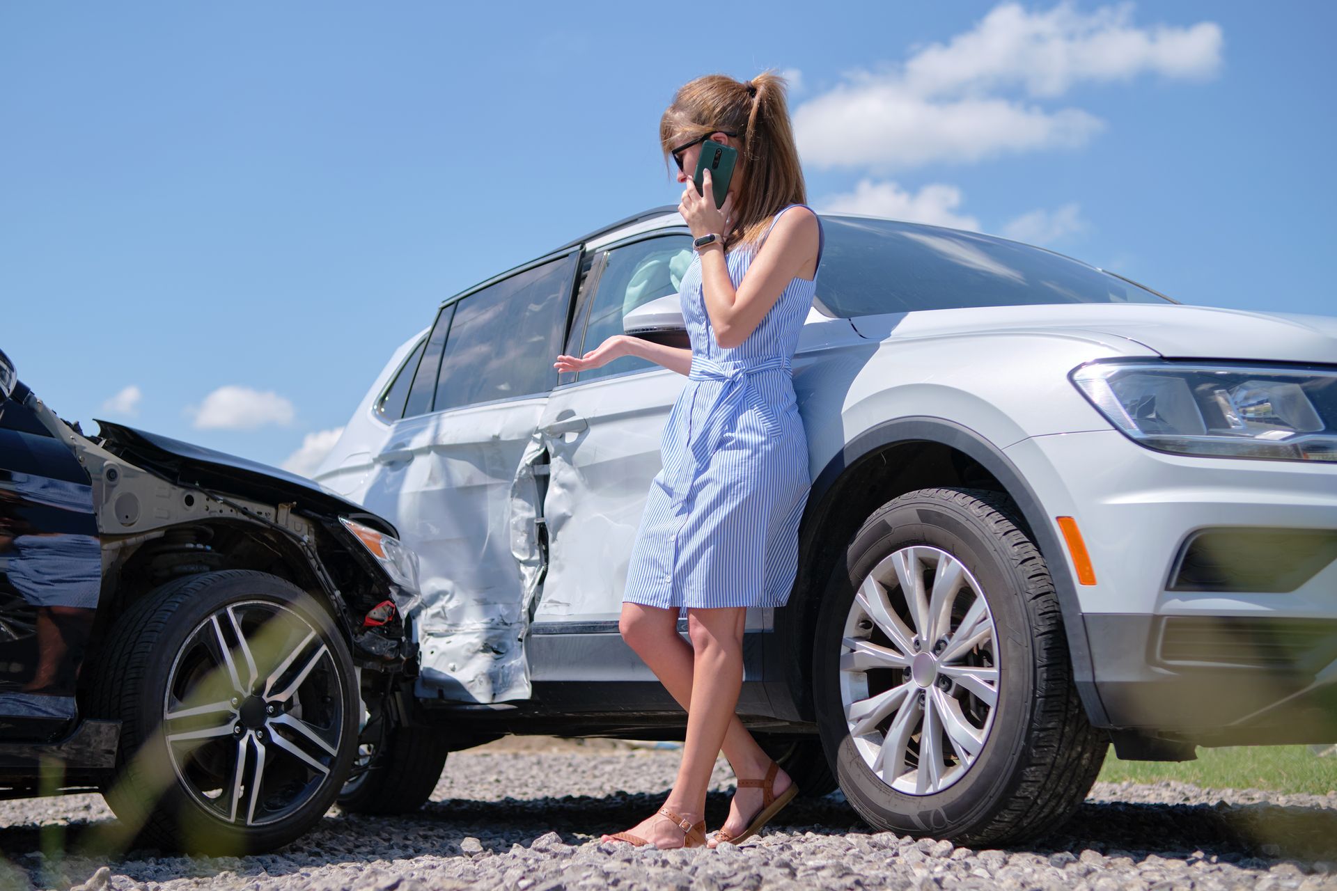A woman is standing next to a damaged car talking on a cell phone.