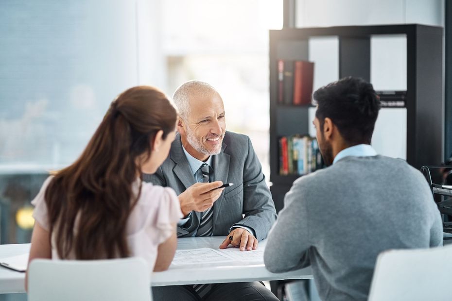 A man and a woman are sitting at a table talking to a man in a suit.