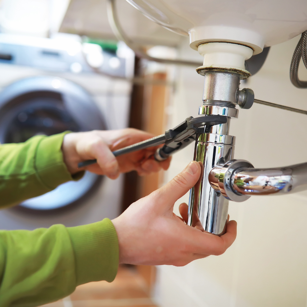 Person using a wrench to repair plumbing under a sink.