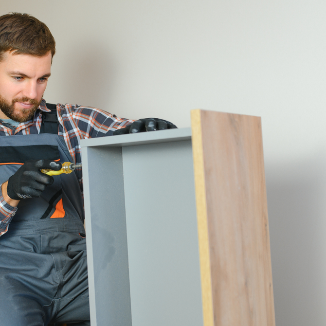 Person in work overalls assembling a cabinet with a screwdriver indoors.