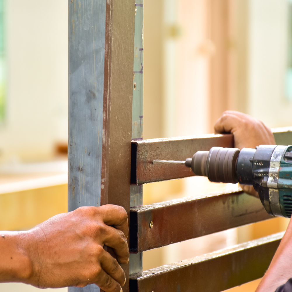 Person drilling into a metal fence, possibly during installation.