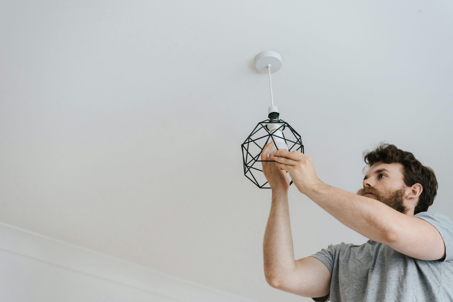 Man installs a black wireframe pendant light fixture on a white ceiling.