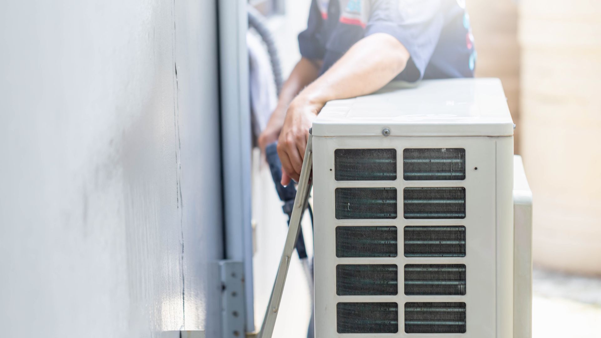 A person installs an air conditioner unit on a wall outside.