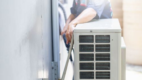 A person installs an air conditioner unit on a wall outside.