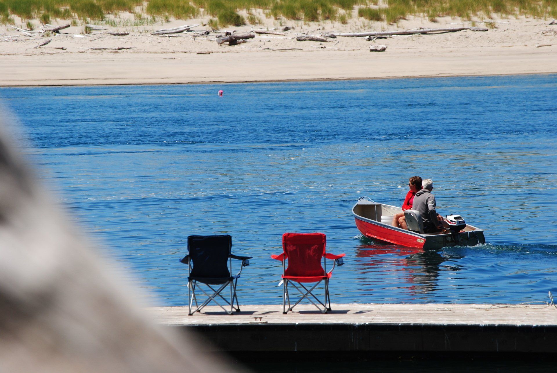 Two chairs are sitting on a dock next to a boat in the water.