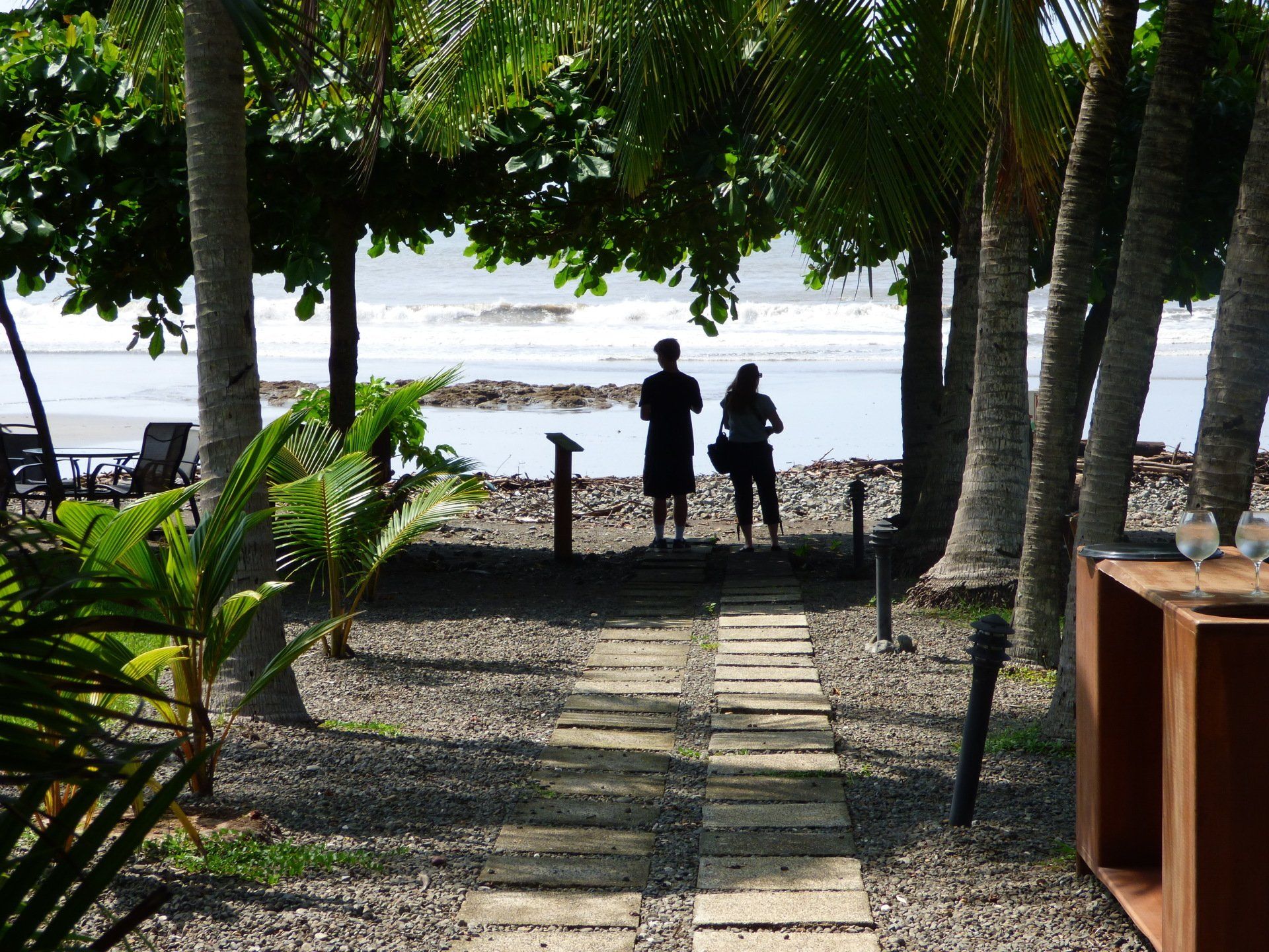 Two people are standing on a path looking at the ocean.