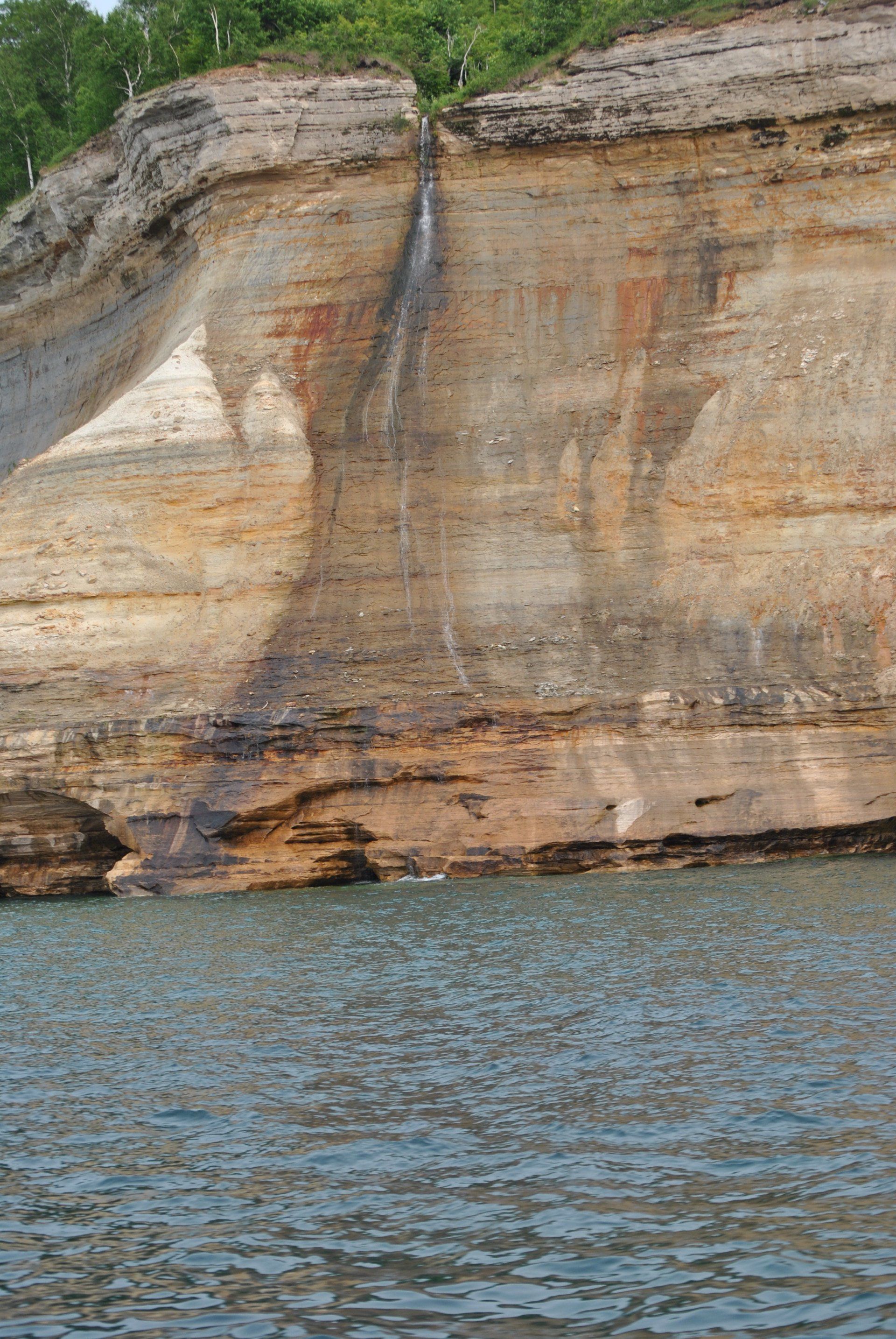 A waterfall is coming down a cliff into a body of water.