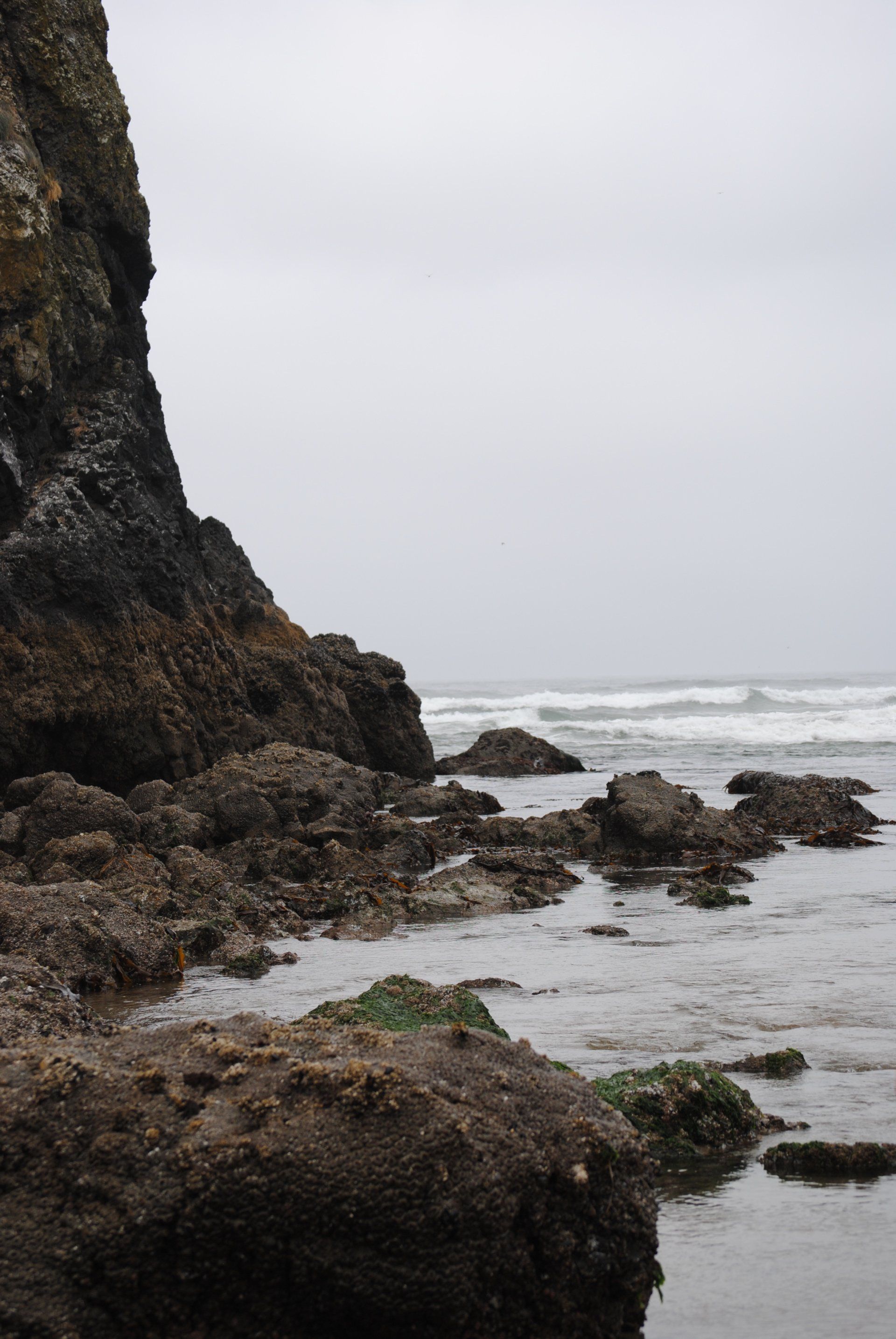 A rocky beach with a large rock in the foreground and a large rock in the background.