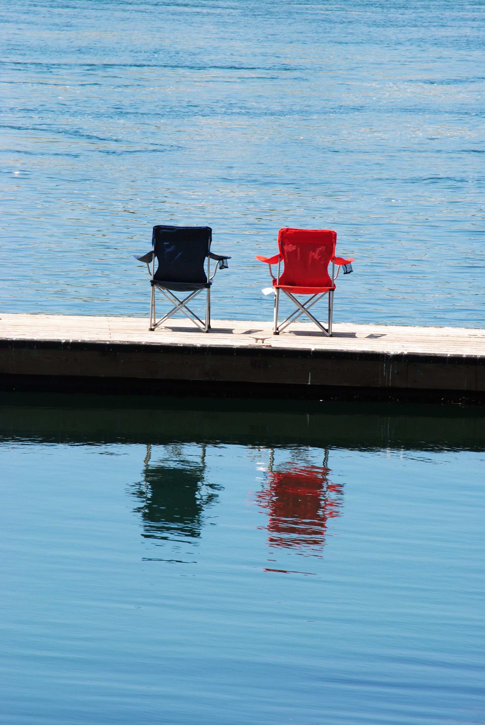 Two folding chairs are sitting on a dock overlooking a body of water.