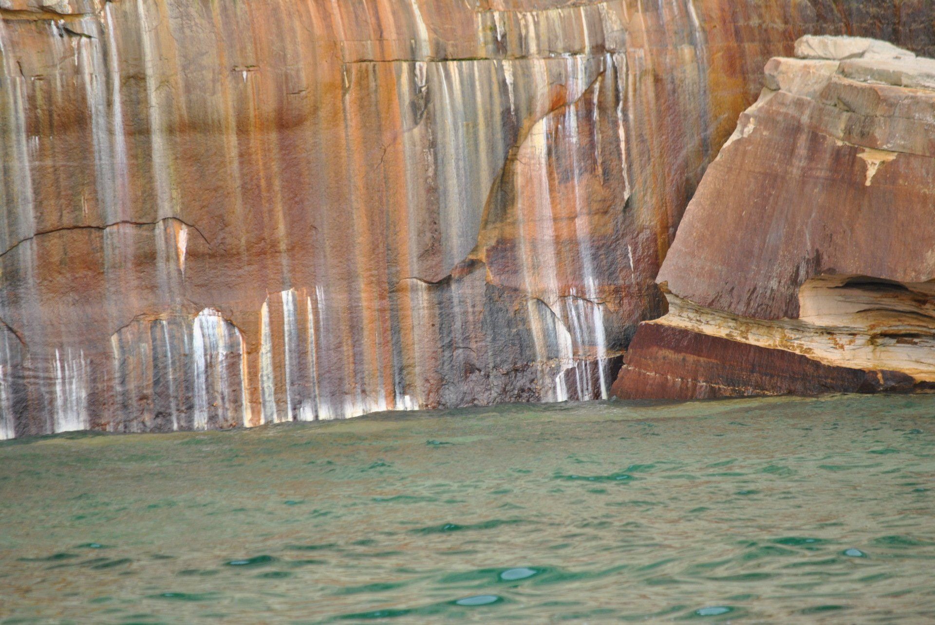 A waterfall is coming down a rock wall next to a body of water.