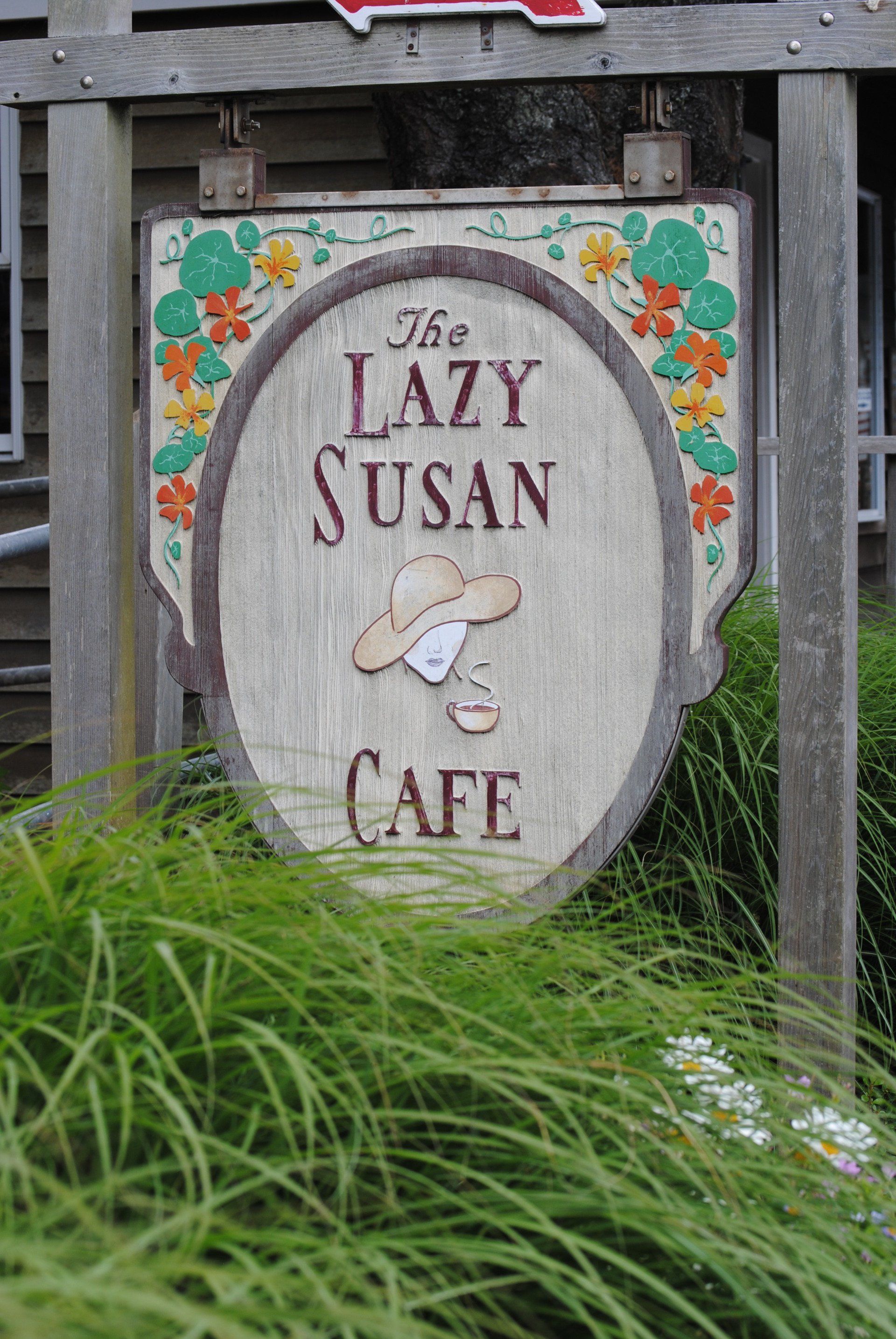 A sign for the lazy susan cafe is surrounded by tall grass.