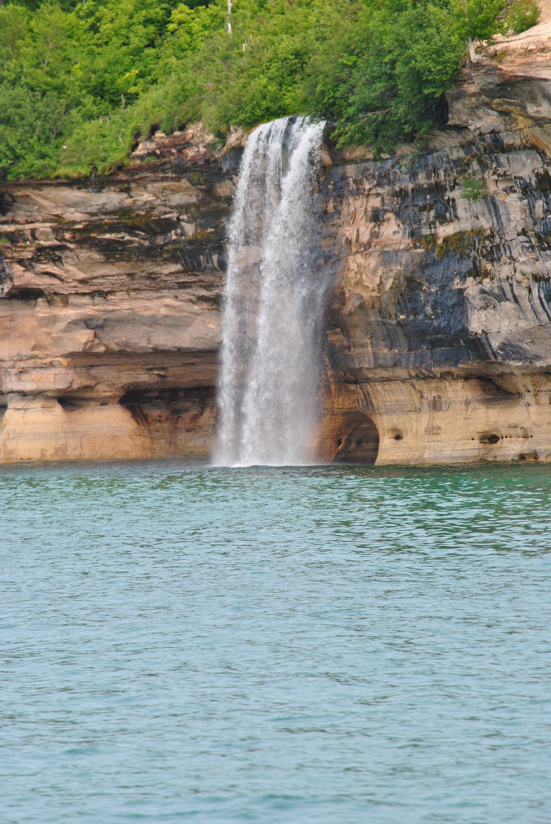A waterfall is coming down a cliff into a body of water.