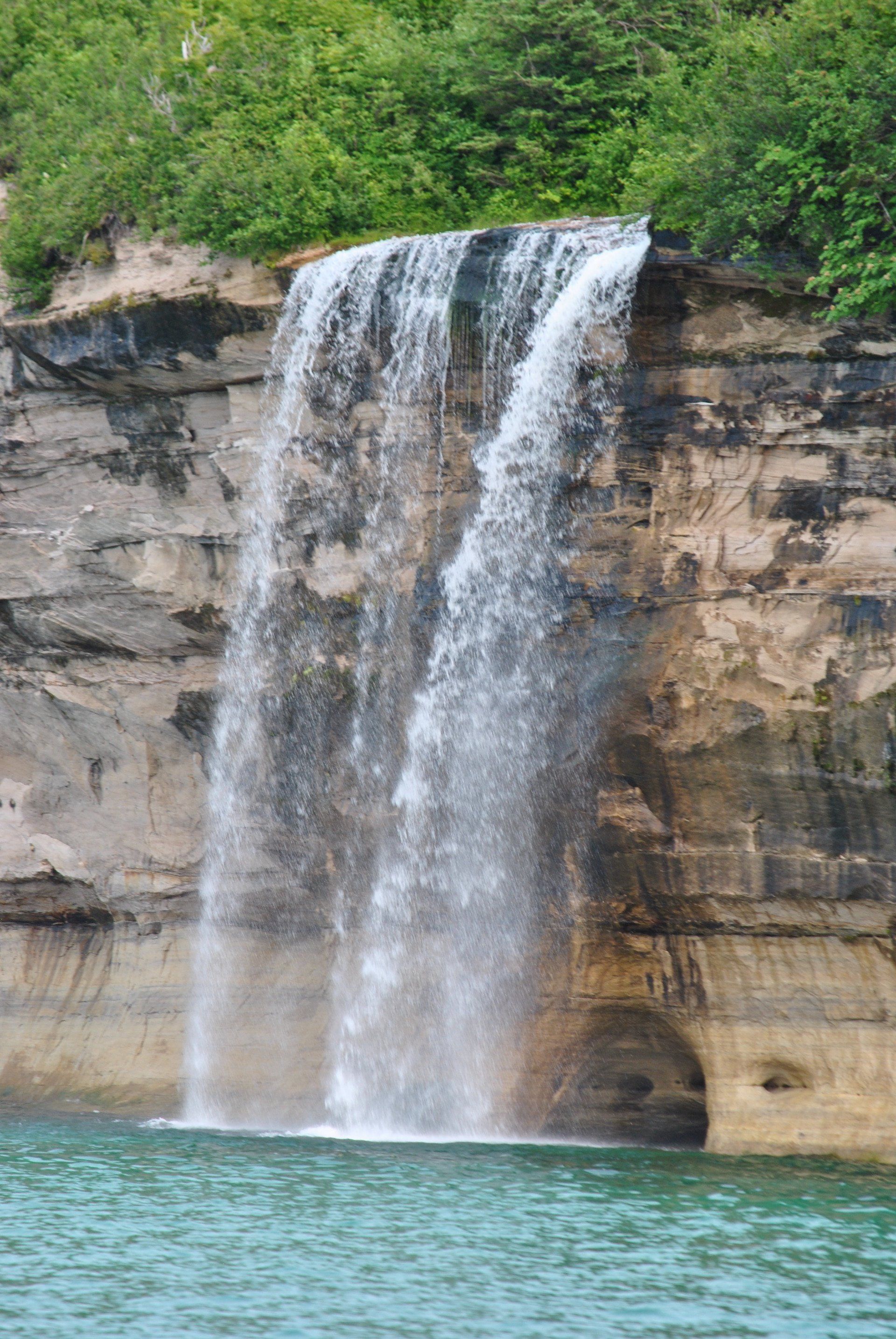 A waterfall is coming down a cliff into a body of water.