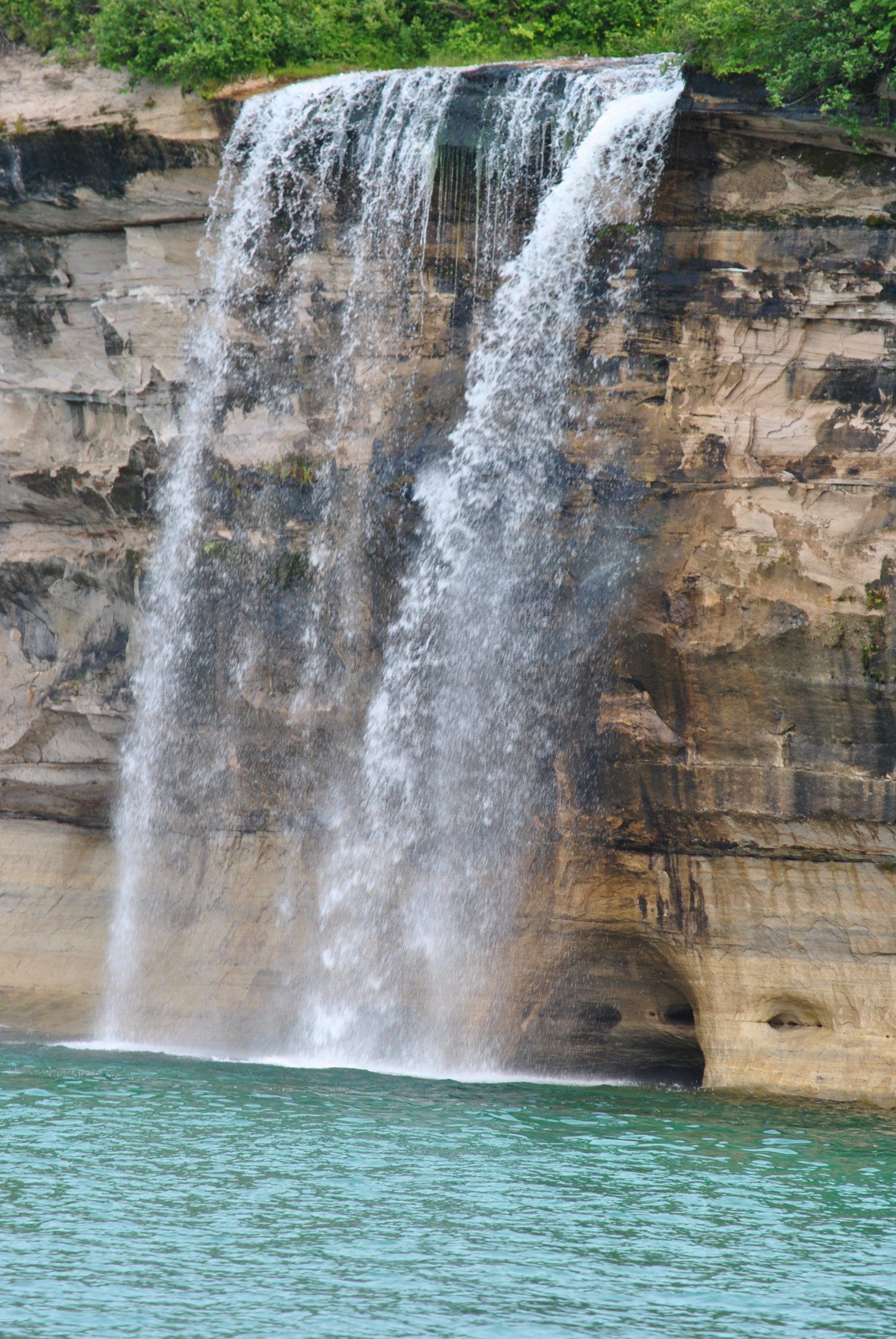 A waterfall is coming down a cliff into a body of water.
