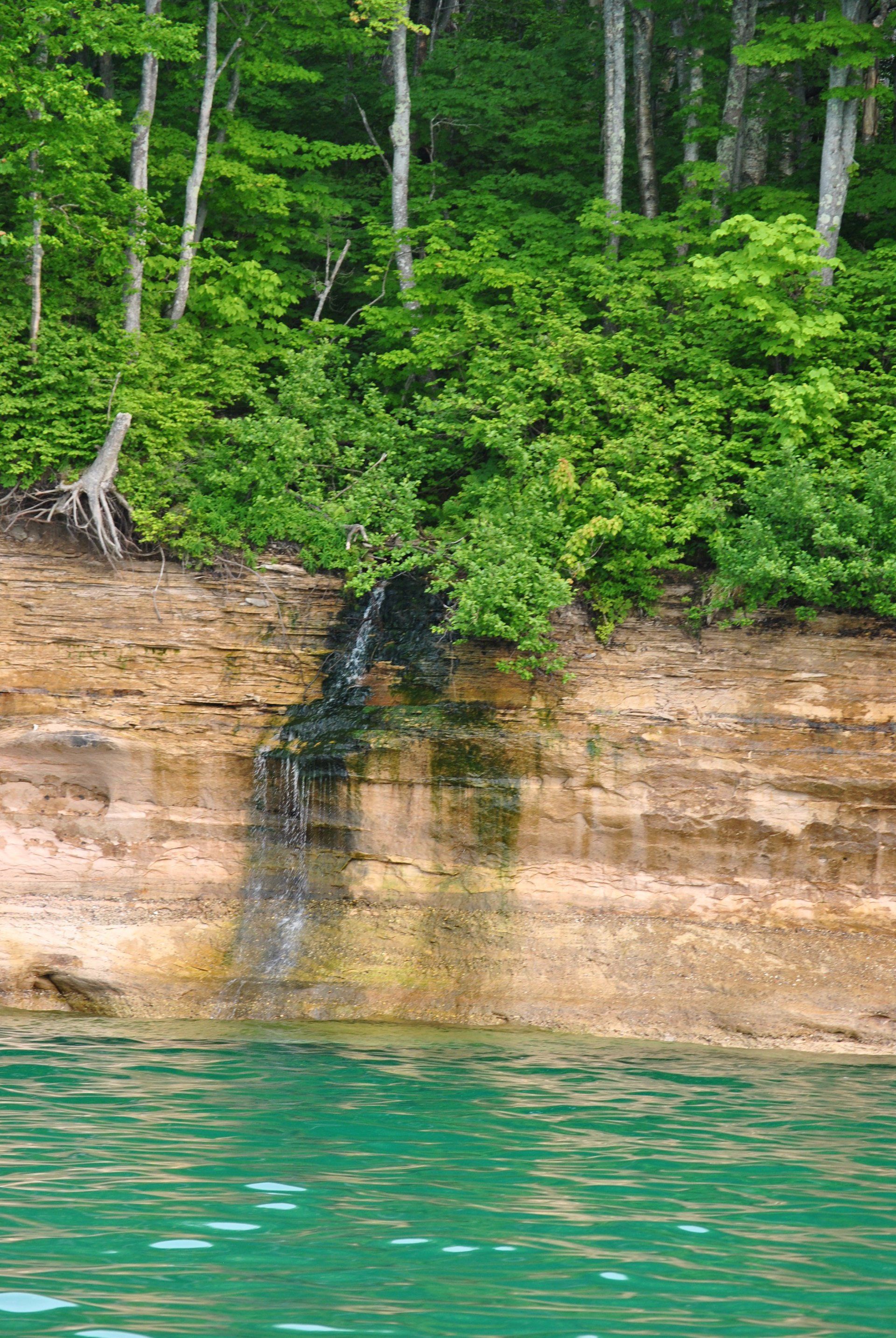 A waterfall is coming down a cliff next to a lake surrounded by trees.