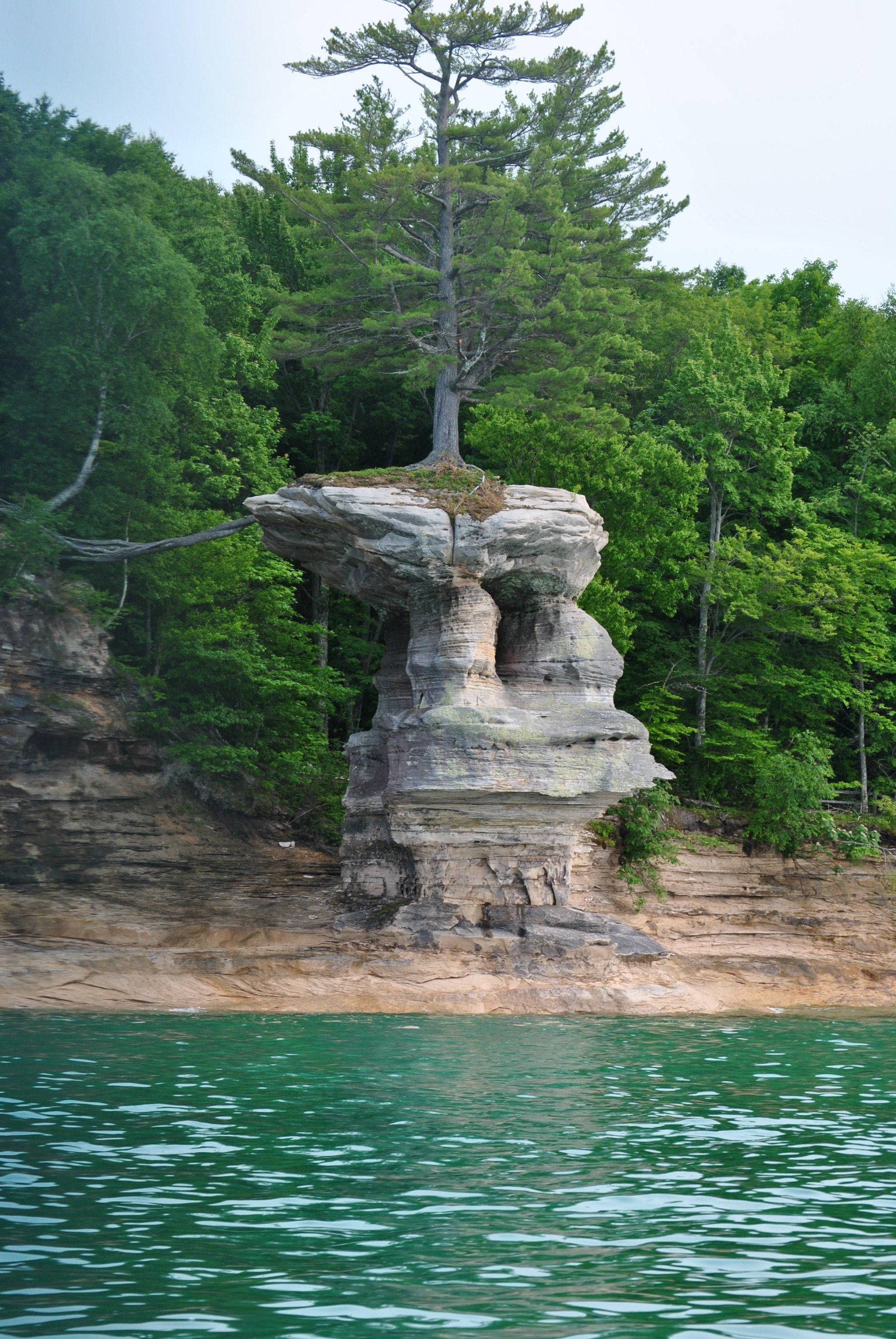 A large rock formation in the middle of a lake surrounded by trees.