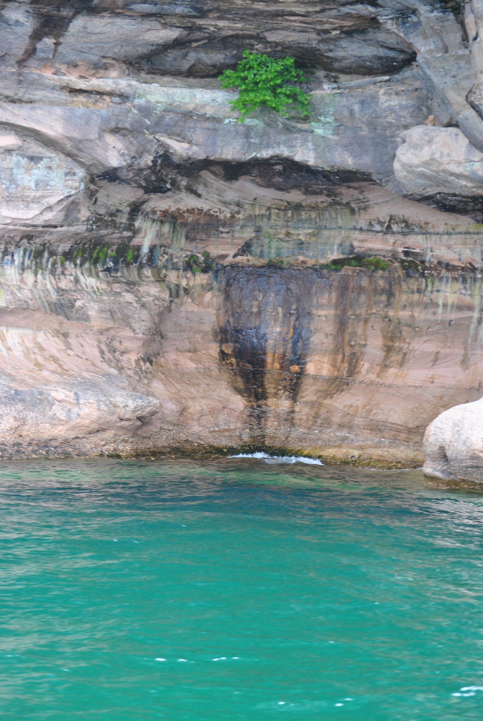 A waterfall is coming out of a rocky cliff next to a body of water.