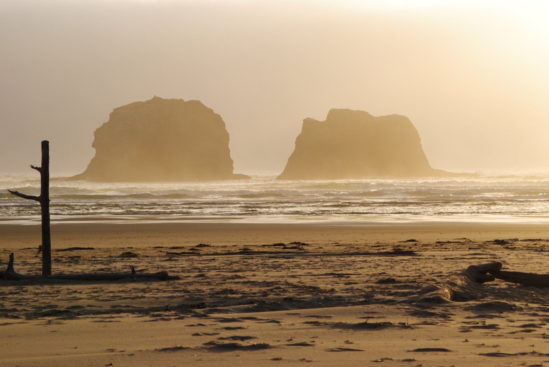 Two large rocks are in the distance on a beach