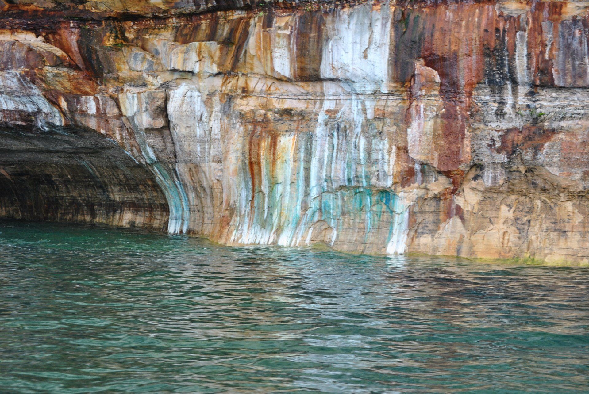 A waterfall is coming out of a cave in the middle of a lake.